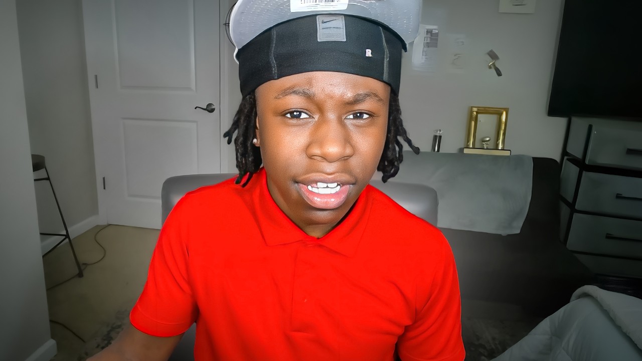 Rakai on stream in a red polo and a black-and-grey cap, speaking to camera from his room.